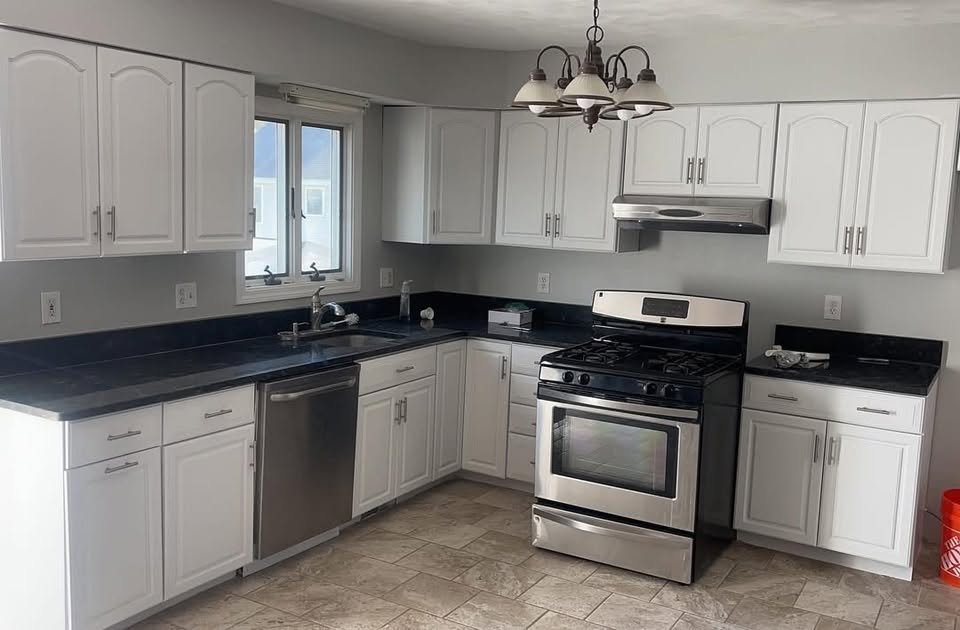 Kitchen with white painted cabinets, dark countertops and a stainless range