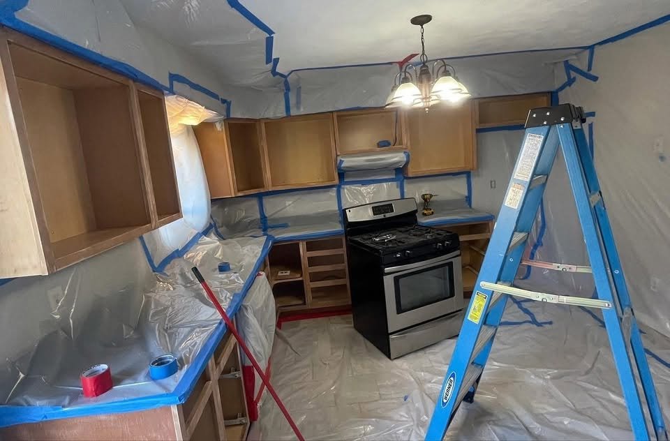 Kitchen masked with plastic and blue tape, cabinet doors removed for painting